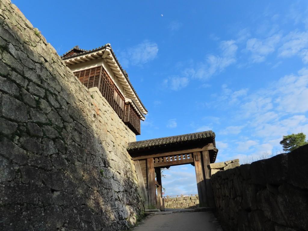 西日差す松山城の石垣と青空の下の戸無門
