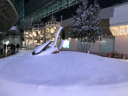 雪に埋もれるやかん - 背景:金沢フォーラス前(金沢駅東口)