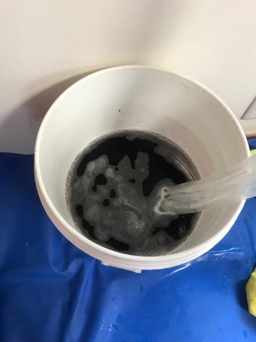エアコンの高圧洗浄による汚水で真っ黒な水がたまるバケツ