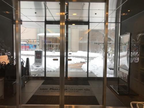 ドーミーイン金沢の出入口の自動ドアの向こうに見える雪景色