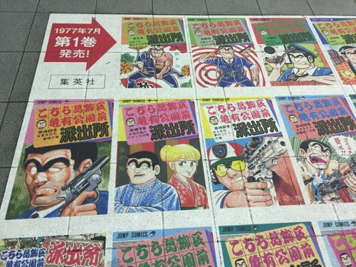 JR亀有駅改札口前の床に貼られたこち亀コミックスの表紙集（第1巻、第2巻など）