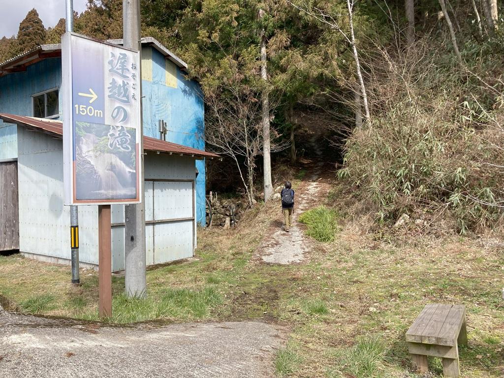 遅越の滝の看板。山道に向かって行く娘。