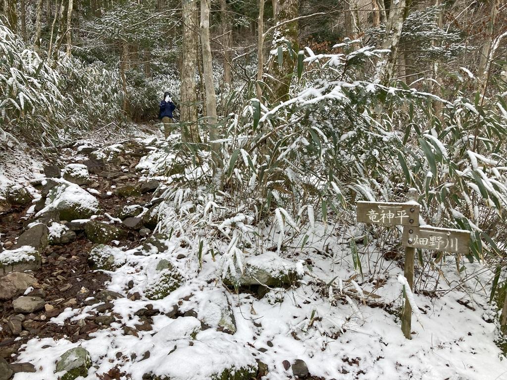 皿ヶ嶺畑野川ルート9：雪の山道から振り向いて撮影する娘、竜神平・畑野川の標識