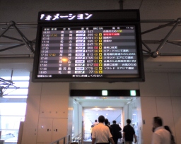 羽田空港第2ターミナルに設置されている運行状況を表示する液晶ディスプレイ、および、搭乗するために飛行機に向かう人々